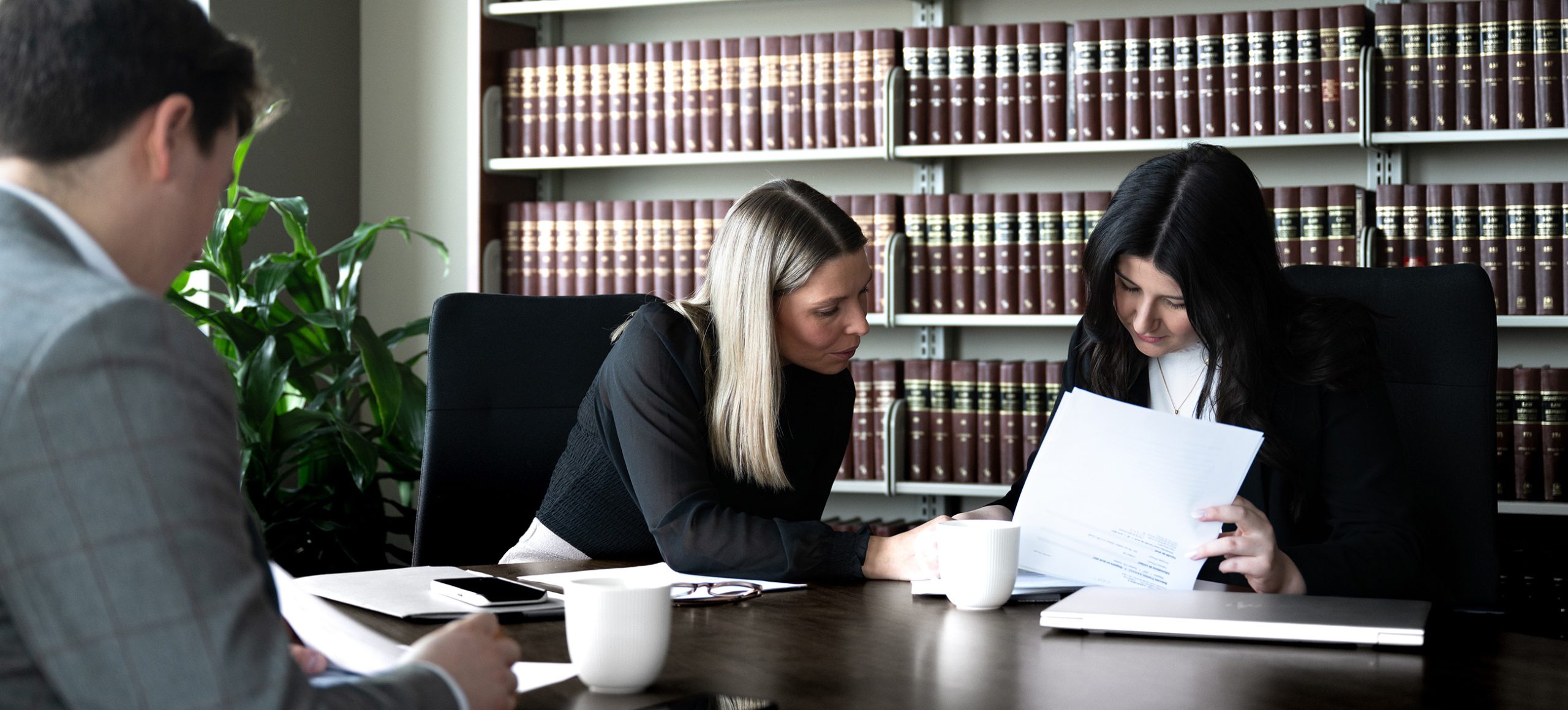 Deux femmes et un homme attablées lisant un document